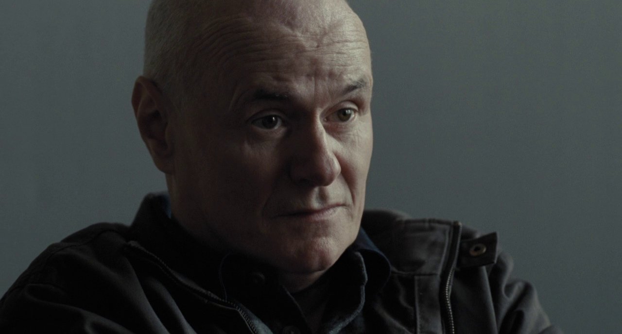 Film still from I, Daniel Blake (2016) showing bald man staring into space by British director Ken Loach