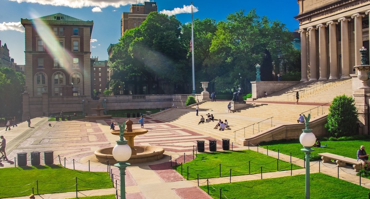 The courtyard of Columbia University on a sunny day with students sitting on the steps