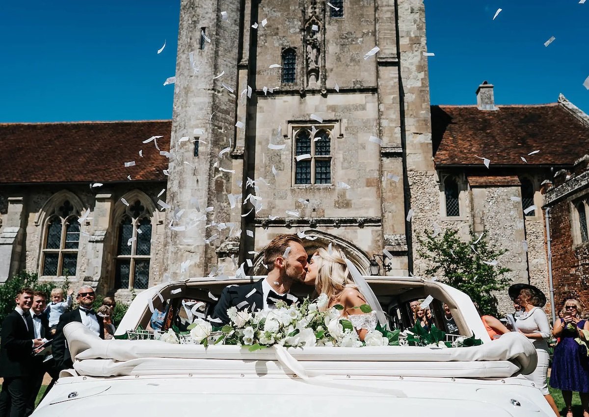 Wedding couple kissing in wedding car outside St Cross chapel
