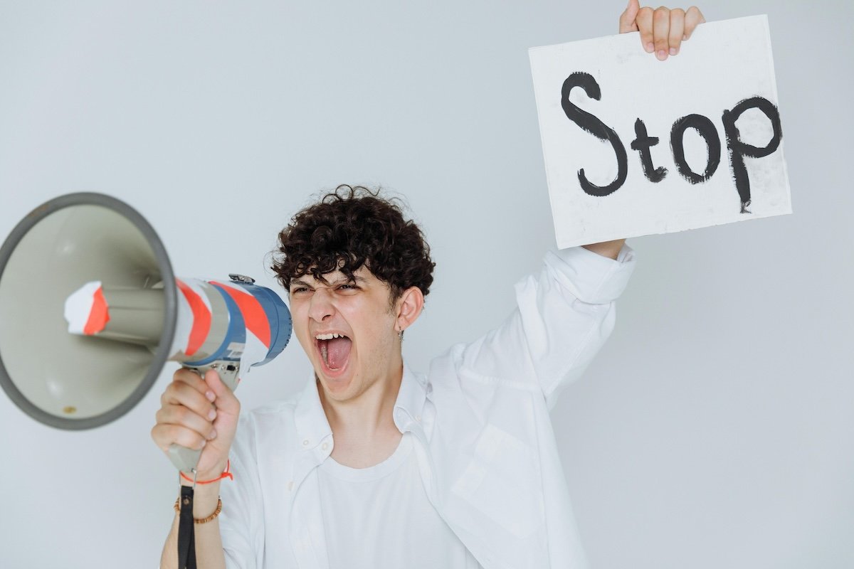 man yelling into megaphone and holding a placard that reads Stop