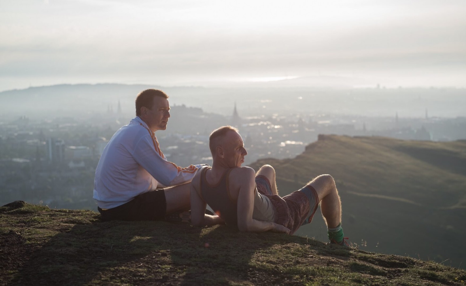 Film still from Trainspotting (1996) showing two men lying on a hill looking out at the Ediburgh skyline